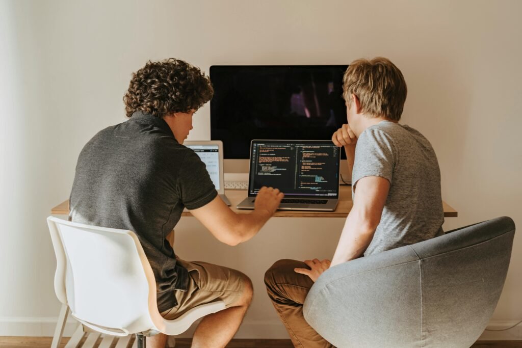 Two men sitting at a table with computers. coding problems, problem-solving skills, algorithms, Frank Berrocal